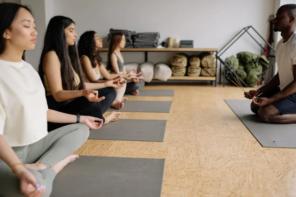 People practicing yoga & meditation in a wellness class with instructor at studio by Dieticiantips